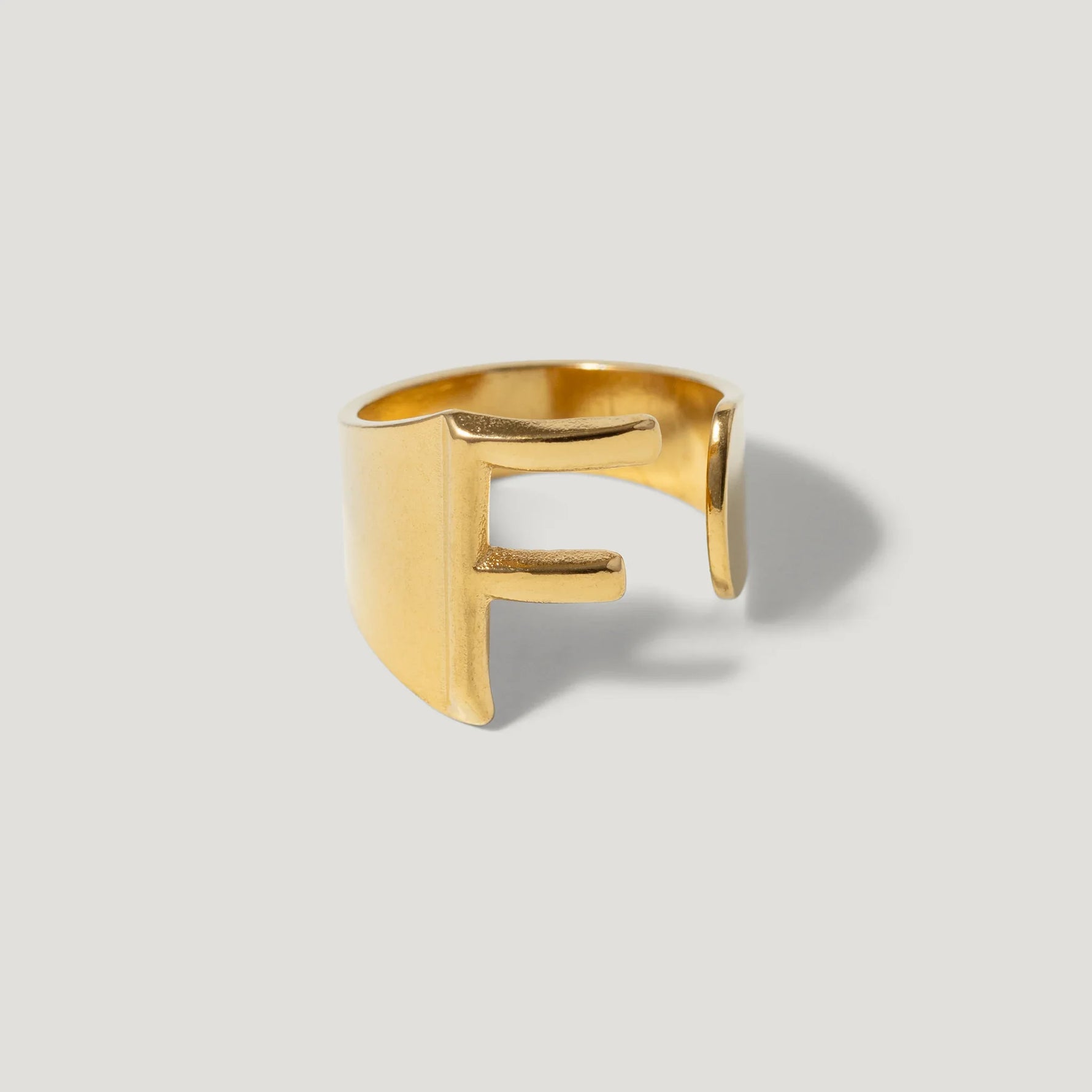 Gold ring with bold letter F design on a light background