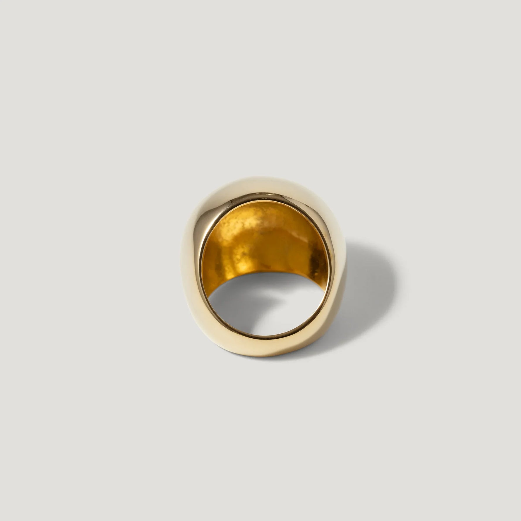 Chunky gold statement ring with smooth, polished finish on a plain light background