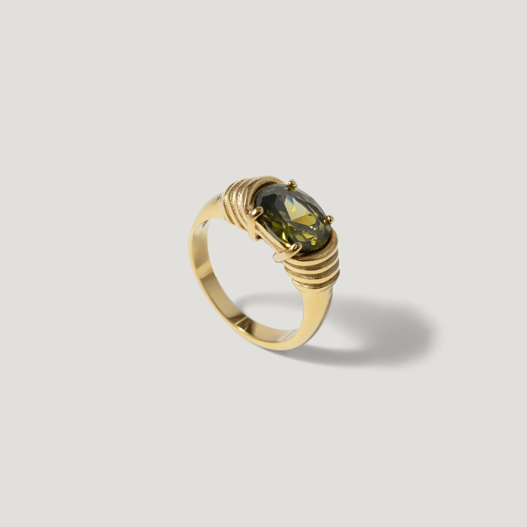 Gold ring with oval green gemstone and intricate wrapped band on neutral background