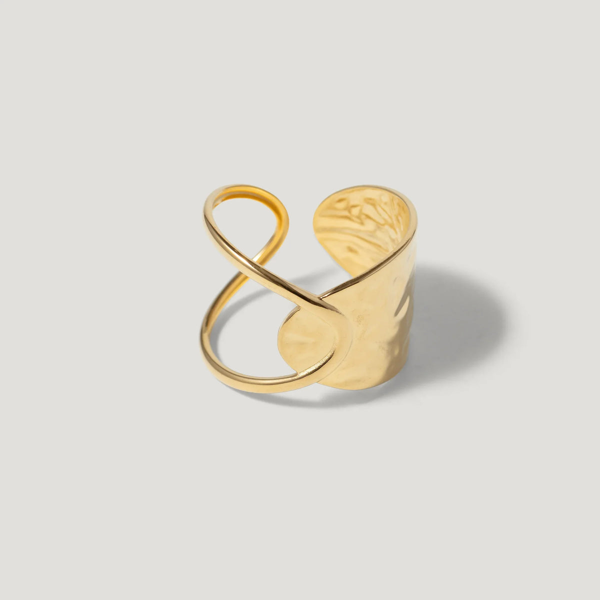 Wide gold cuff ring with abstract, sculptural open design on a light background