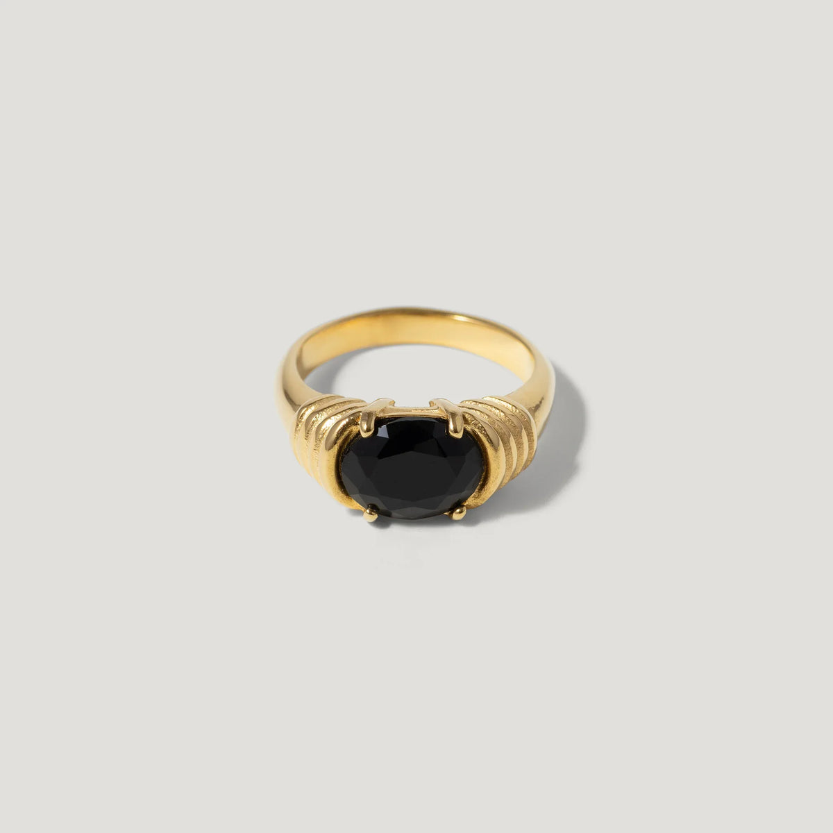 Gold ring with a large round black gemstone and textured band on a light background