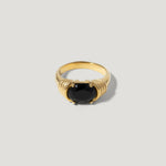 Gold ring with a large round black gemstone and textured band on a light background