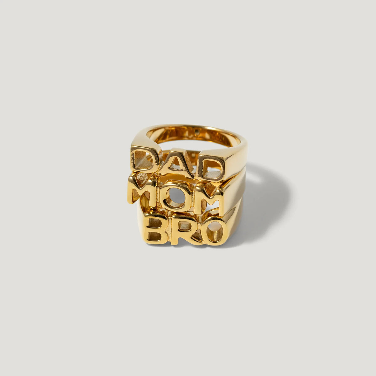 Stacked gold rings with bold letters spelling DAD, MOM, BRO on light background