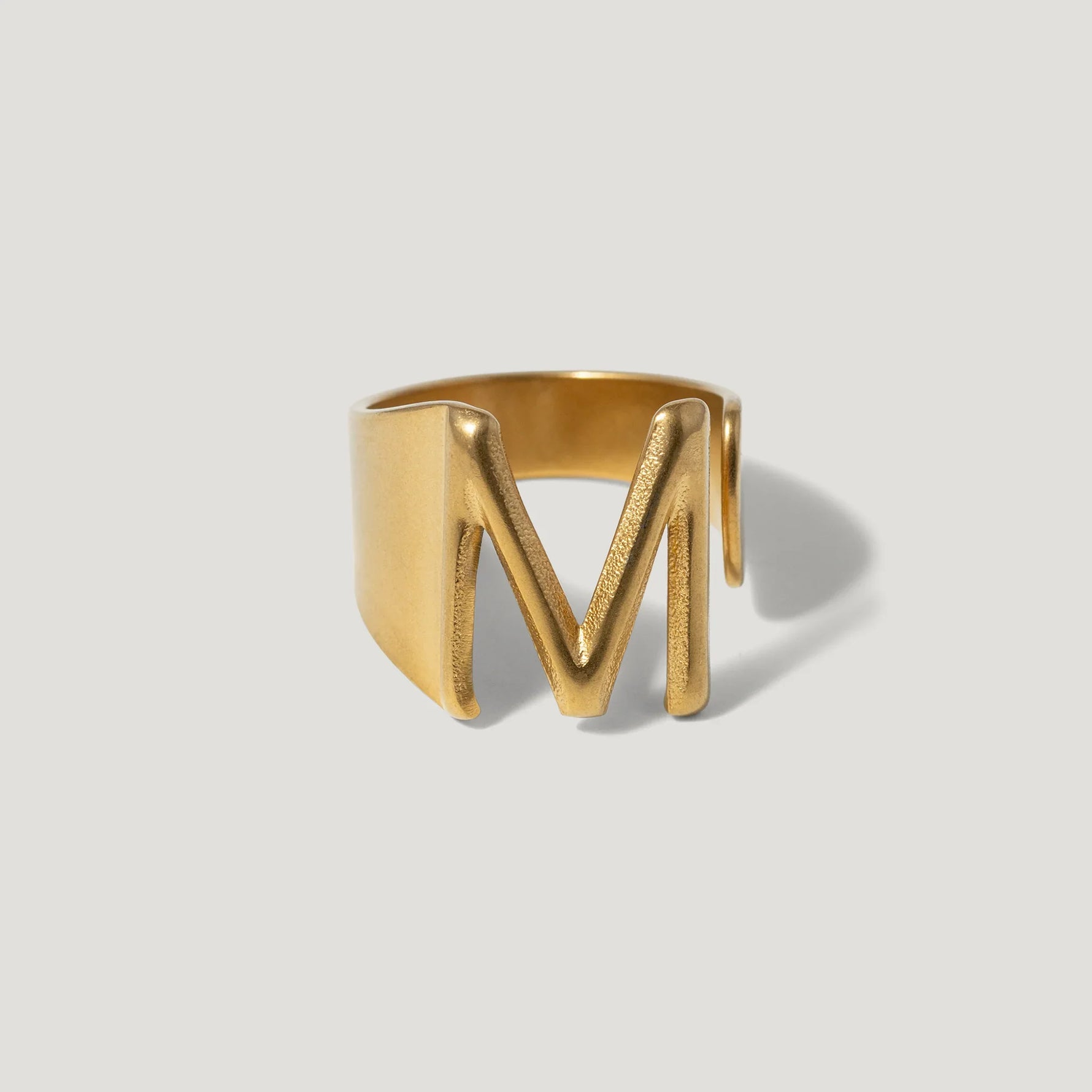 Gold letter M signet ring with bold, modern design on neutral background
