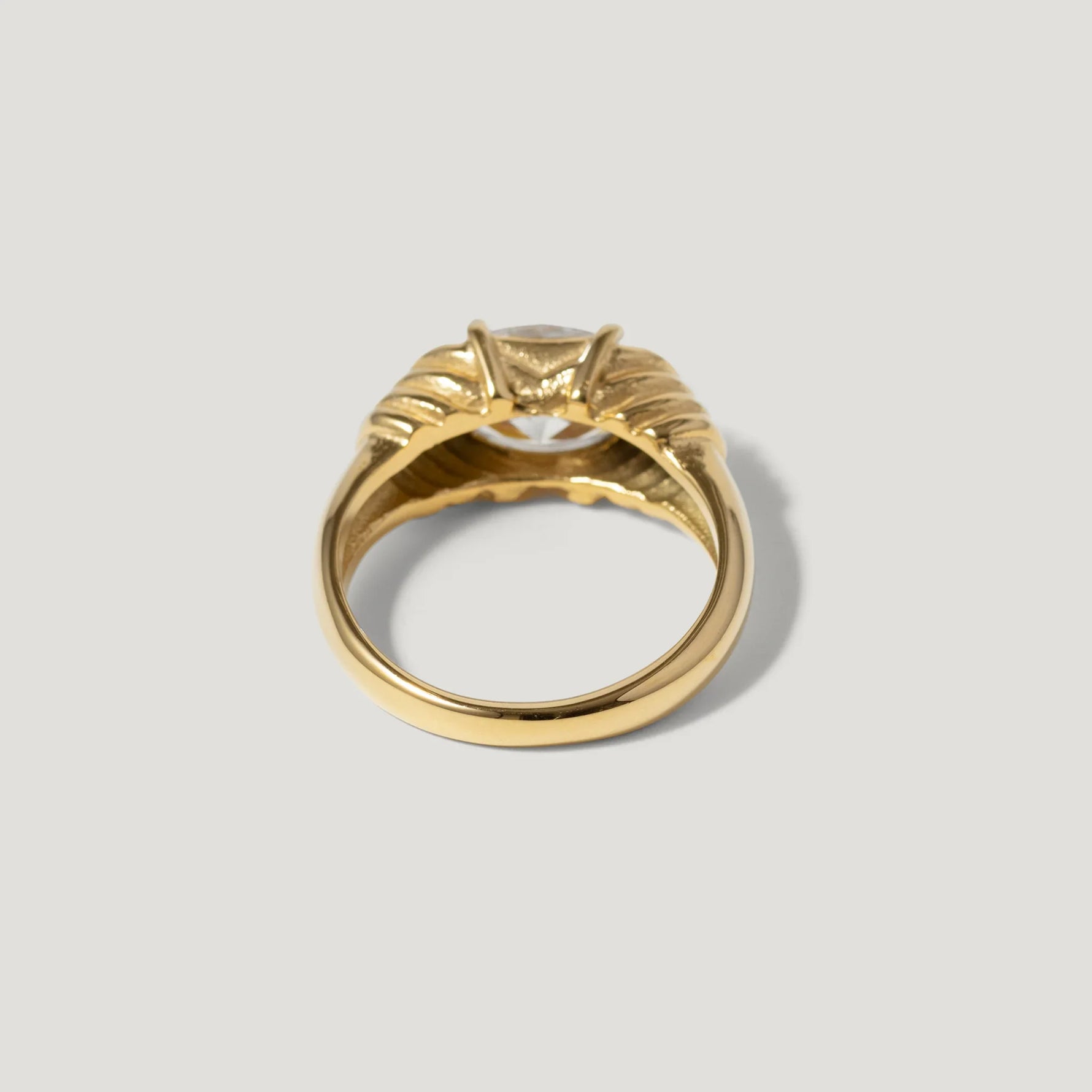 Gold solitaire ring with detailed band and prong-set gemstone on light background