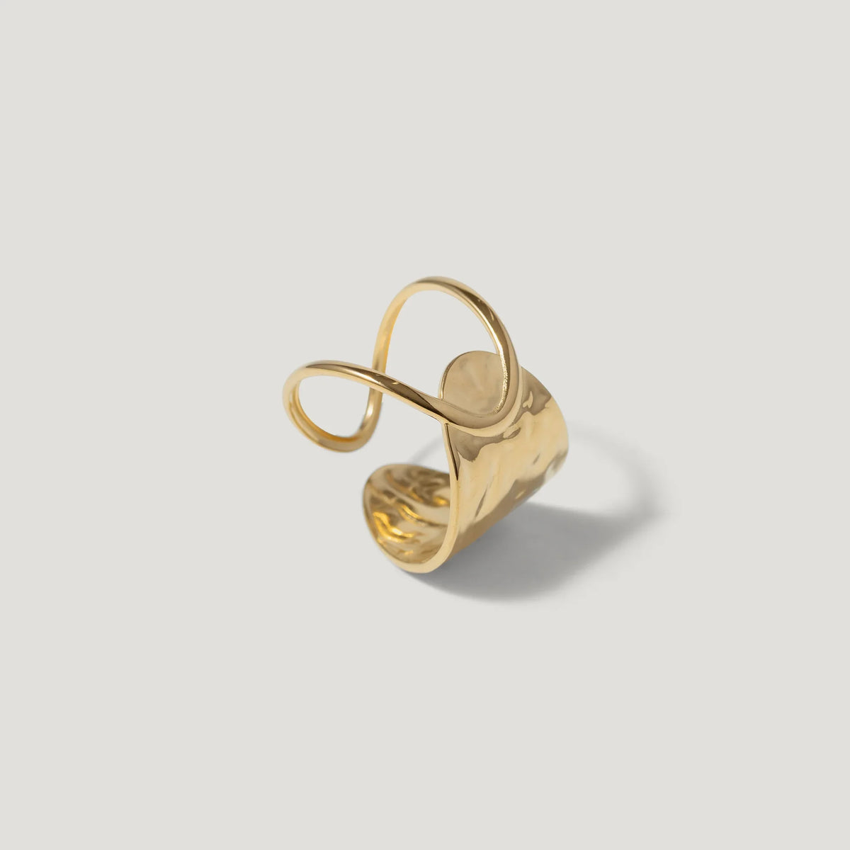 Abstract gold statement ring with organic curves and hammered texture on a white background