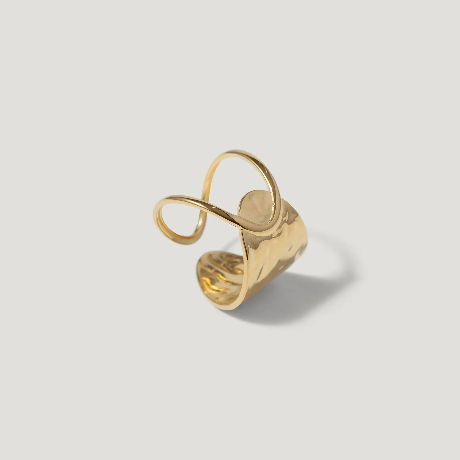 Abstract gold statement ring with organic curves and hammered texture on a white background