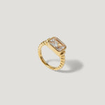 Gold ring with rectangular clear gemstone and twisted band on light background