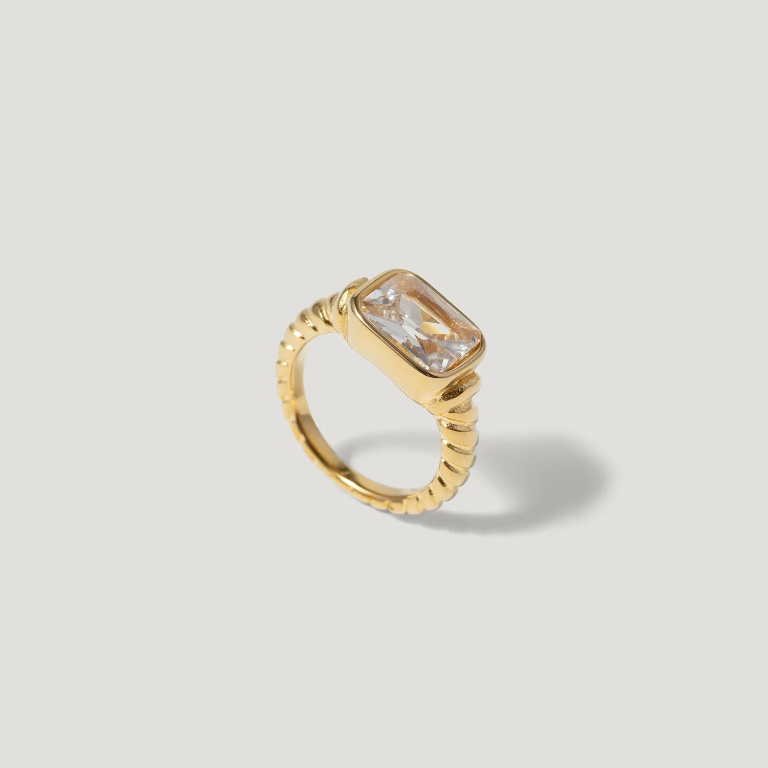 Gold ring with rectangular clear gemstone and twisted band on light background