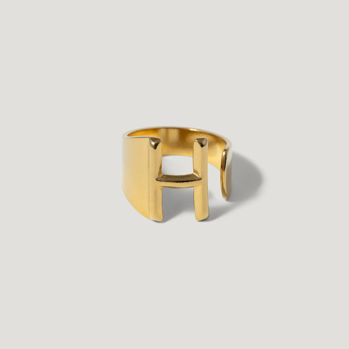 Gold open band ring with bold geometric H-shaped design on neutral background