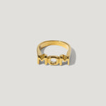 Gold ring with bold 'MOM' lettering on a plain background, modern jewelry design