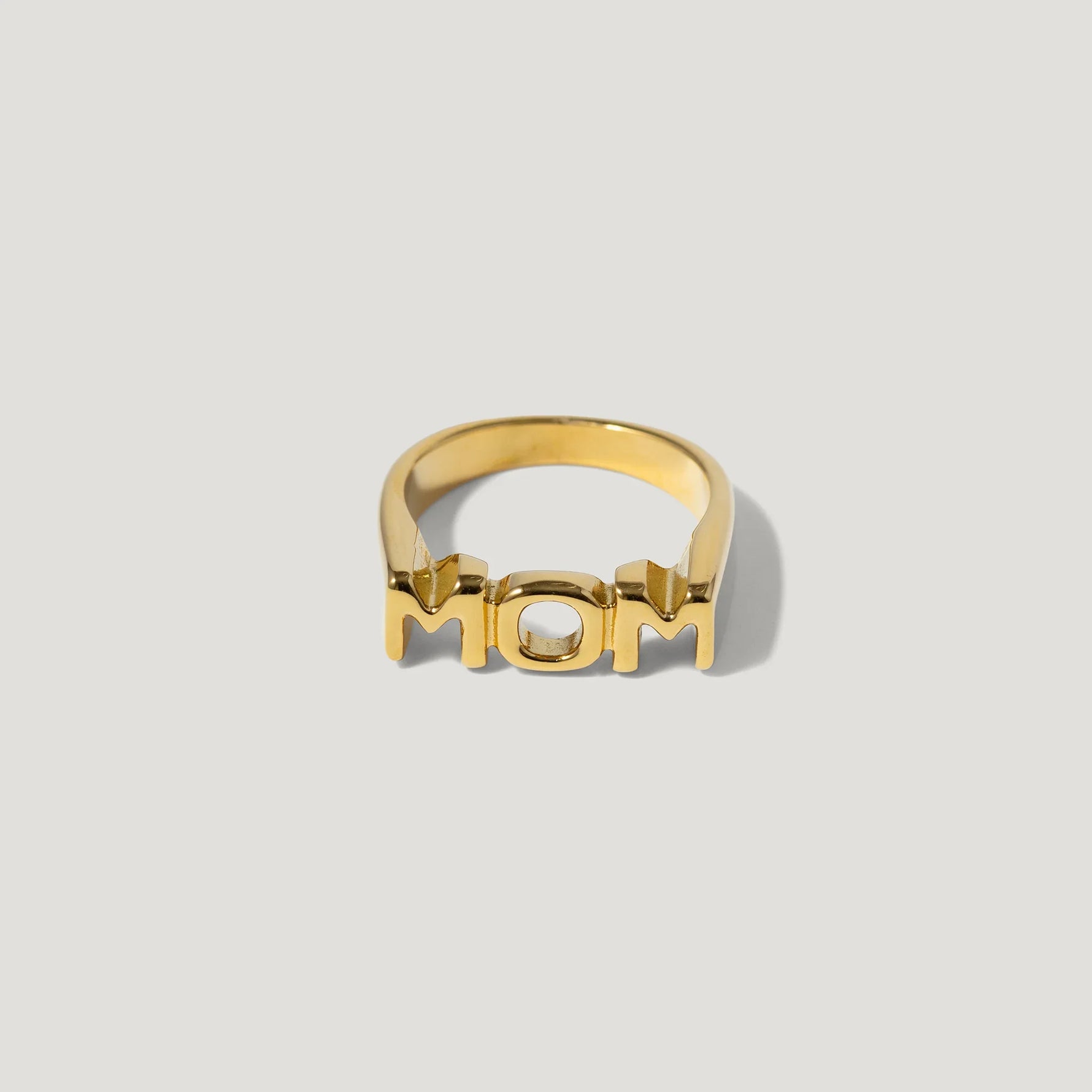 Gold ring with bold 'MOM' lettering on a plain background, modern jewelry design