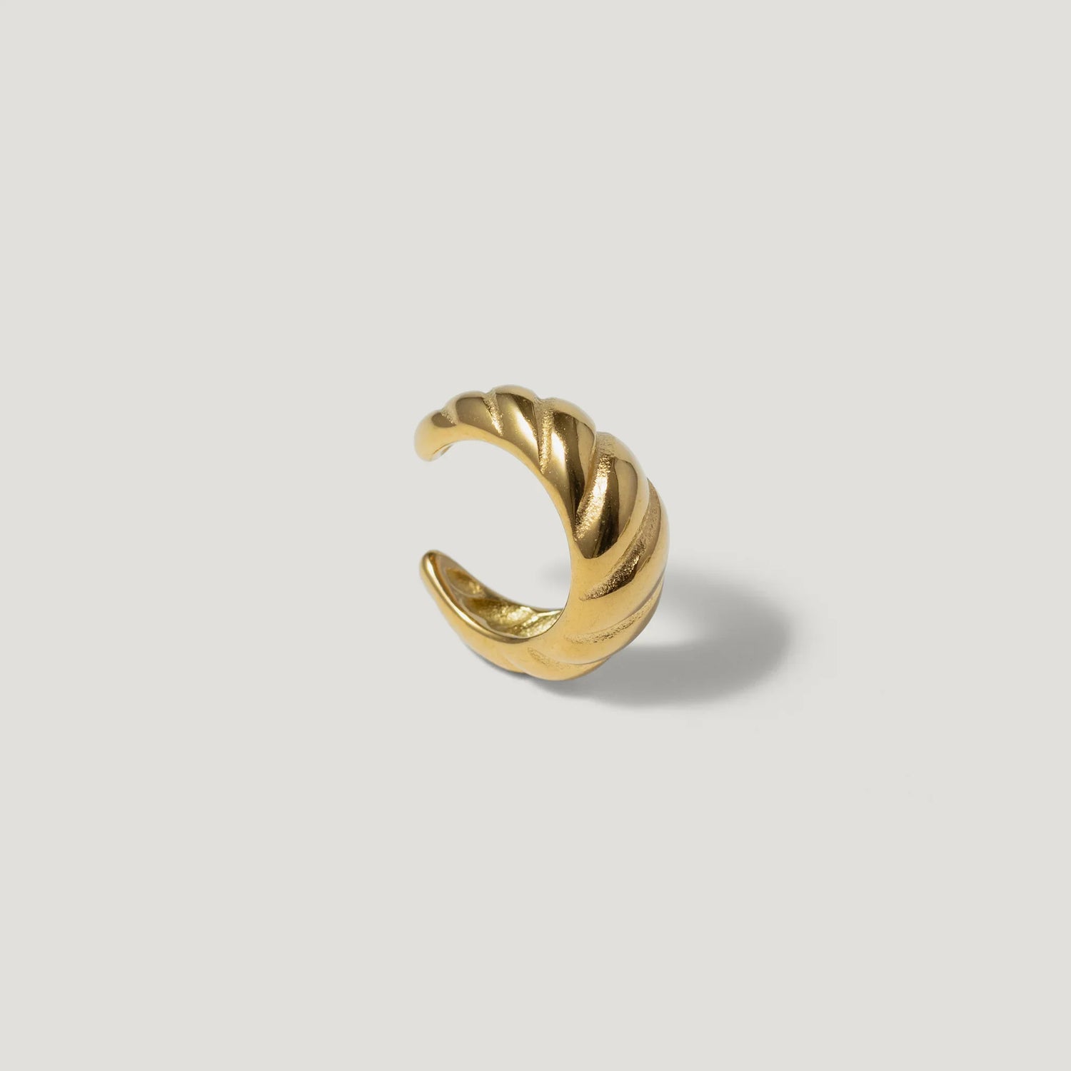 Gold twisted ear cuff with textured design on a light background