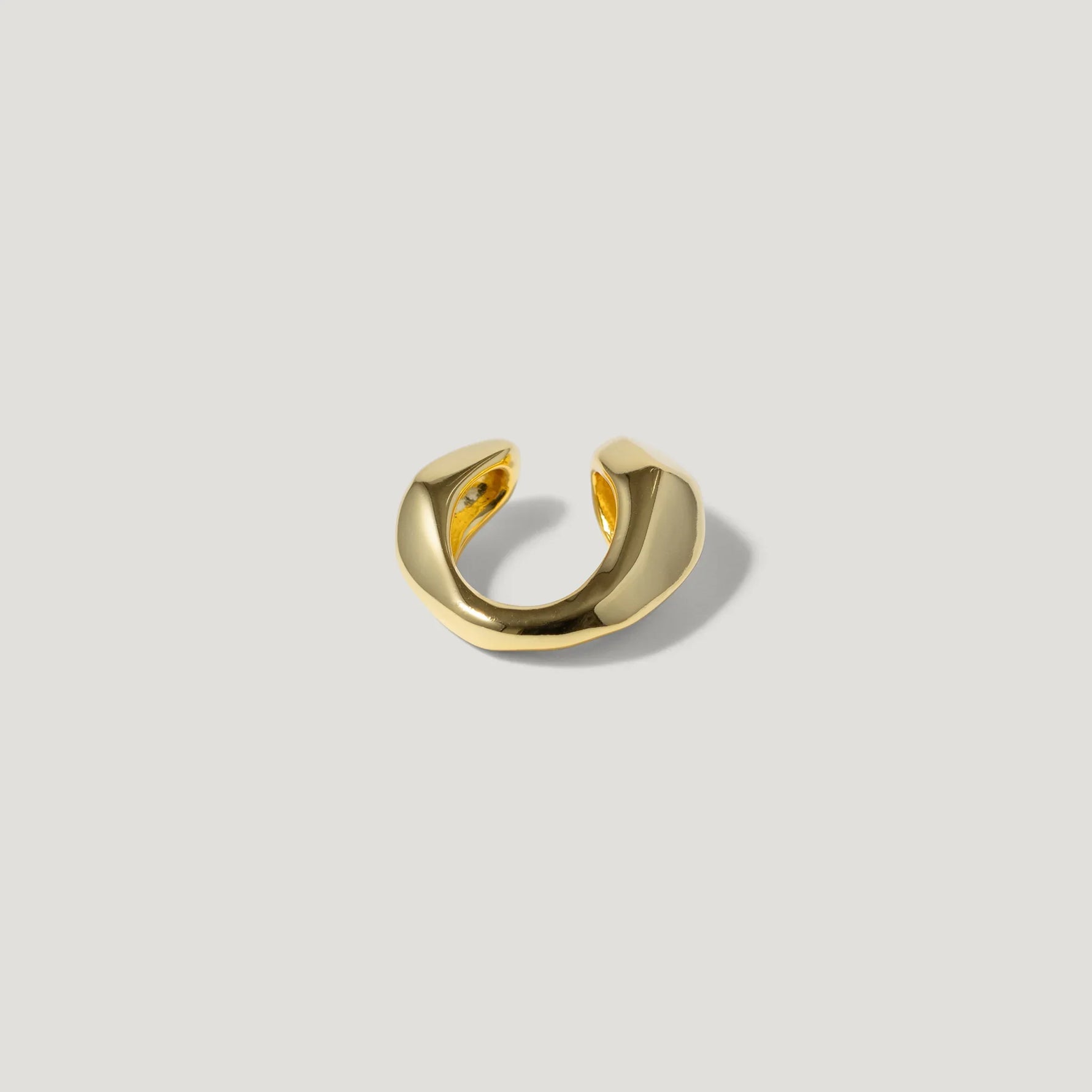 modern gold ear cuff with sculpted design on neutral background