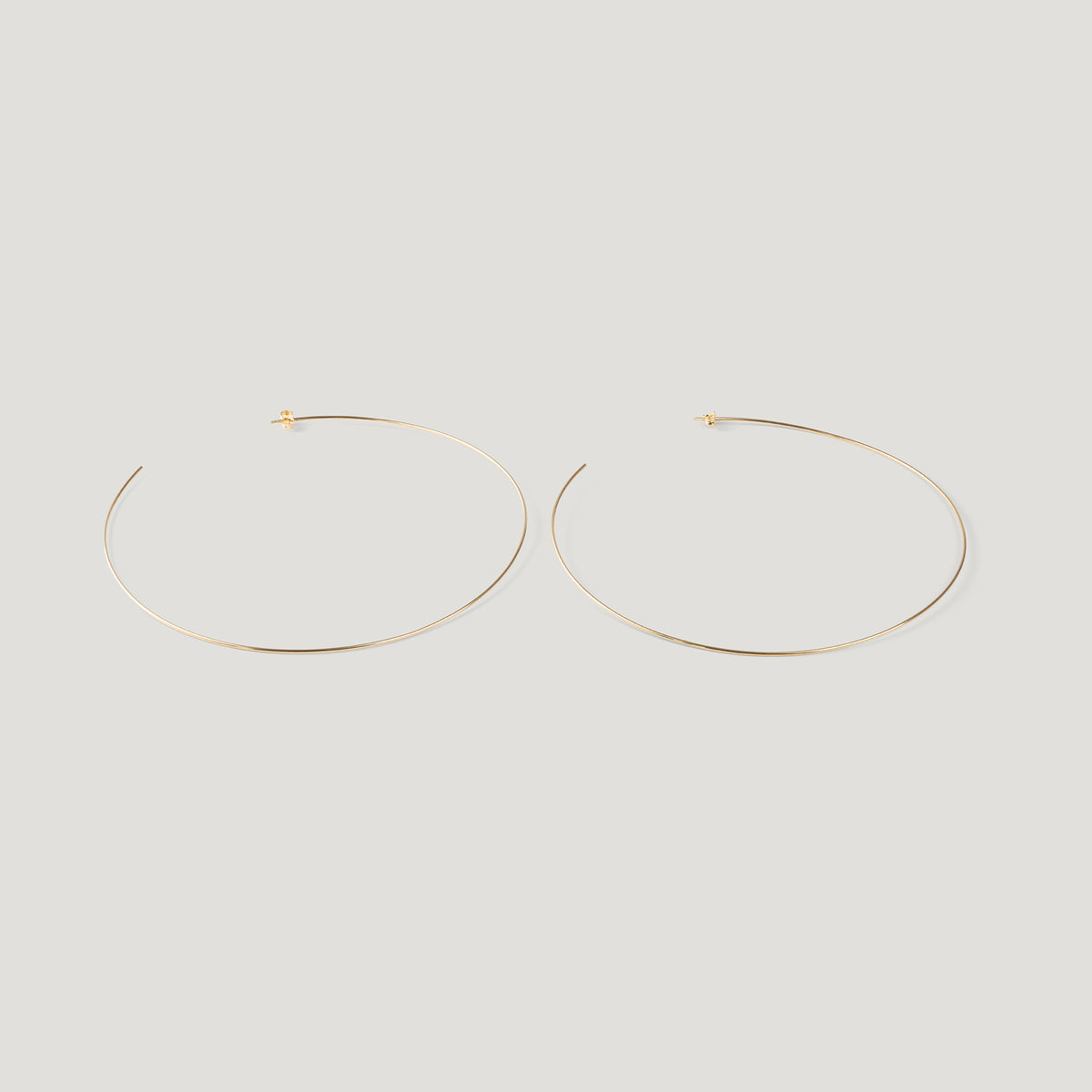Pair of thin gold hoop earrings, laid flat on light background.
