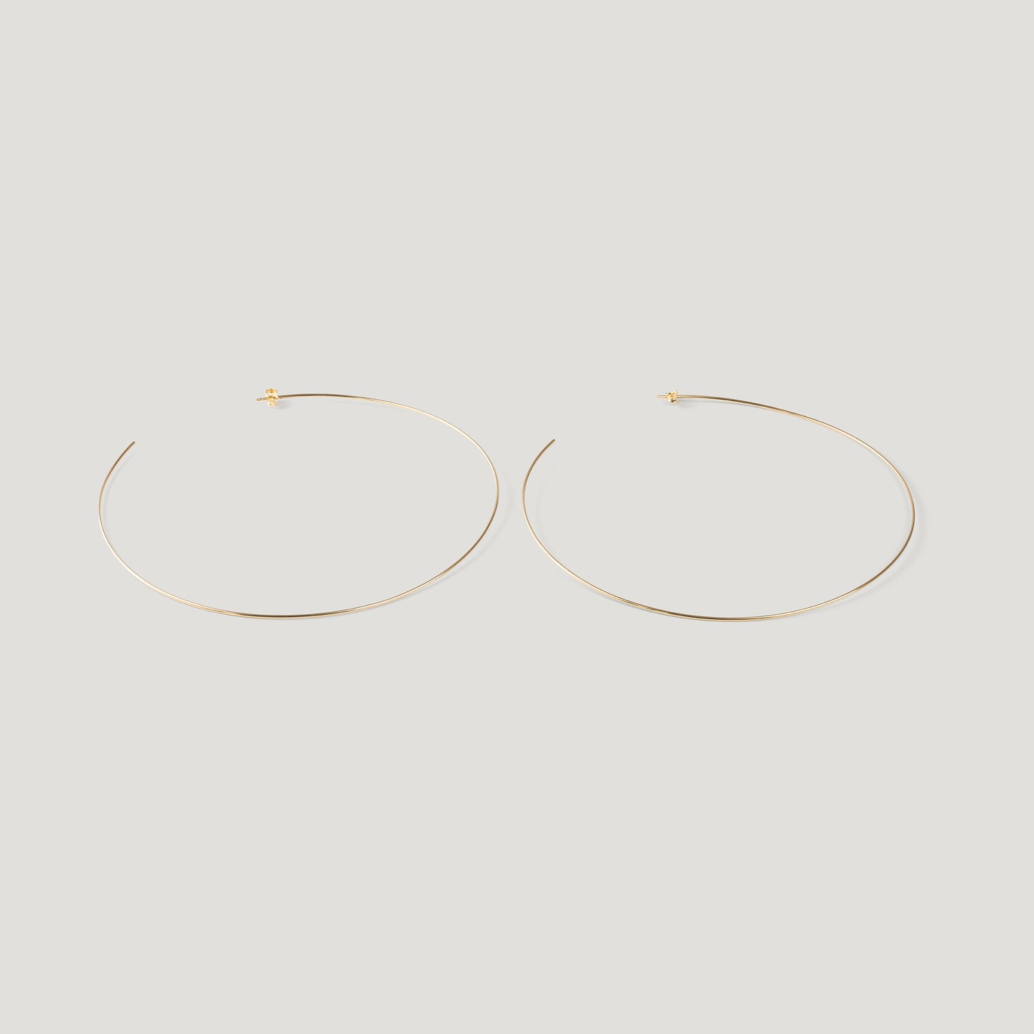 Pair of thin gold hoop earrings, laid flat on light background.