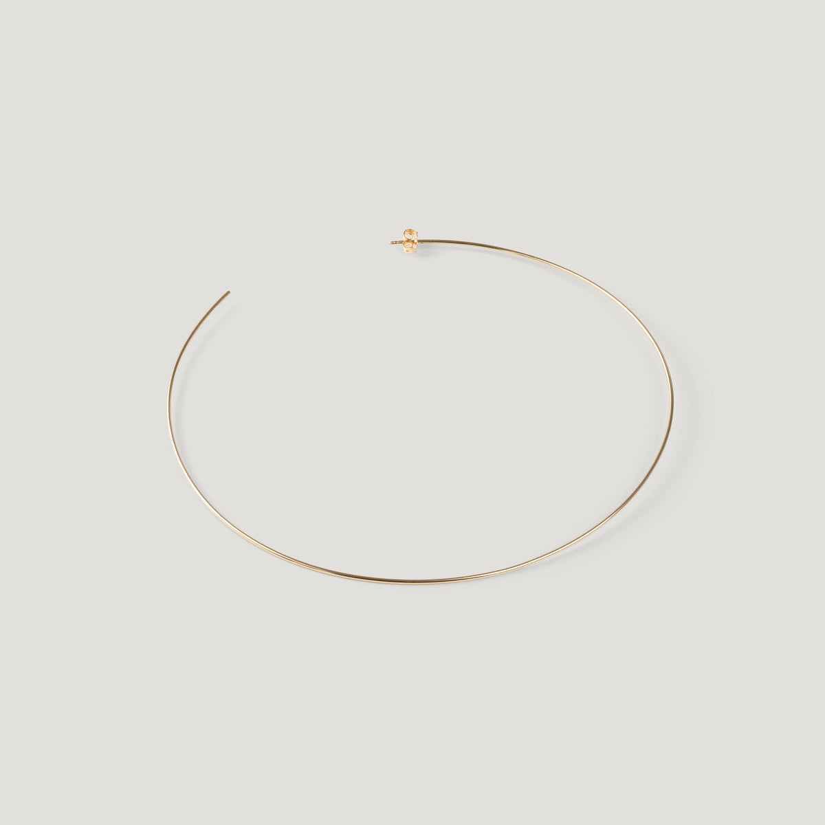 Single gold hoop earring, laid flat and curved on light background.