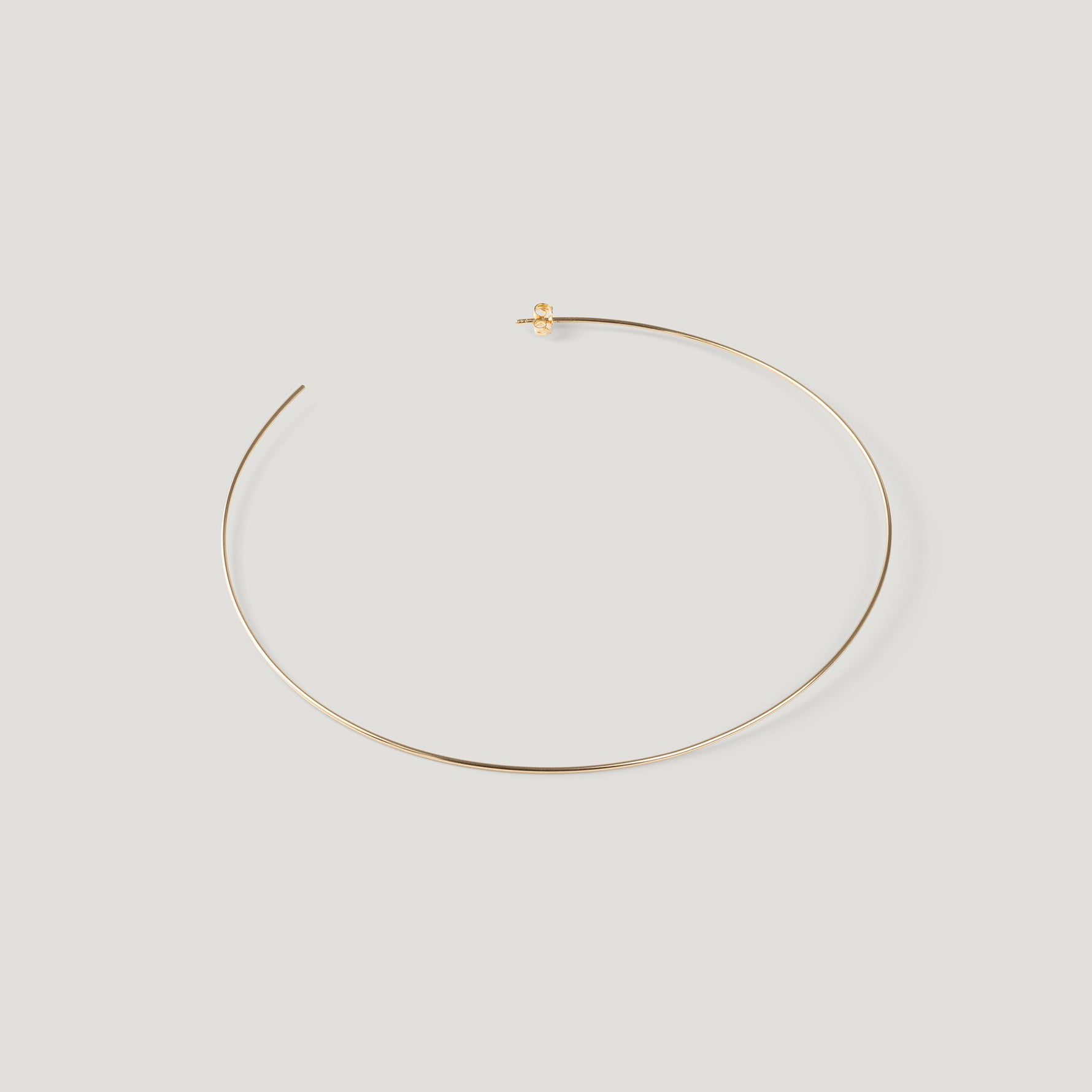 Single gold hoop earring, laid flat and curved on light background.
