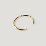 Gold open cuff bangle with rounded wire and ball tip, opening angled to the right.