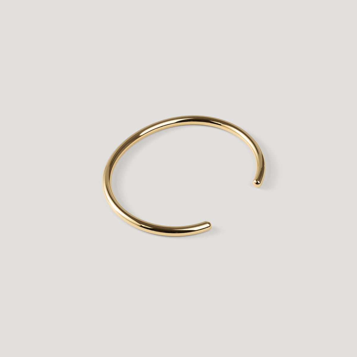 Gold open cuff bangle with rounded wire and ball tip, opening angled to the right.