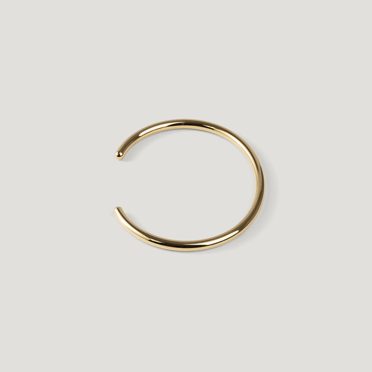 Gold open cuff bangle with rounded wire and ball tip, opening angled to the left.