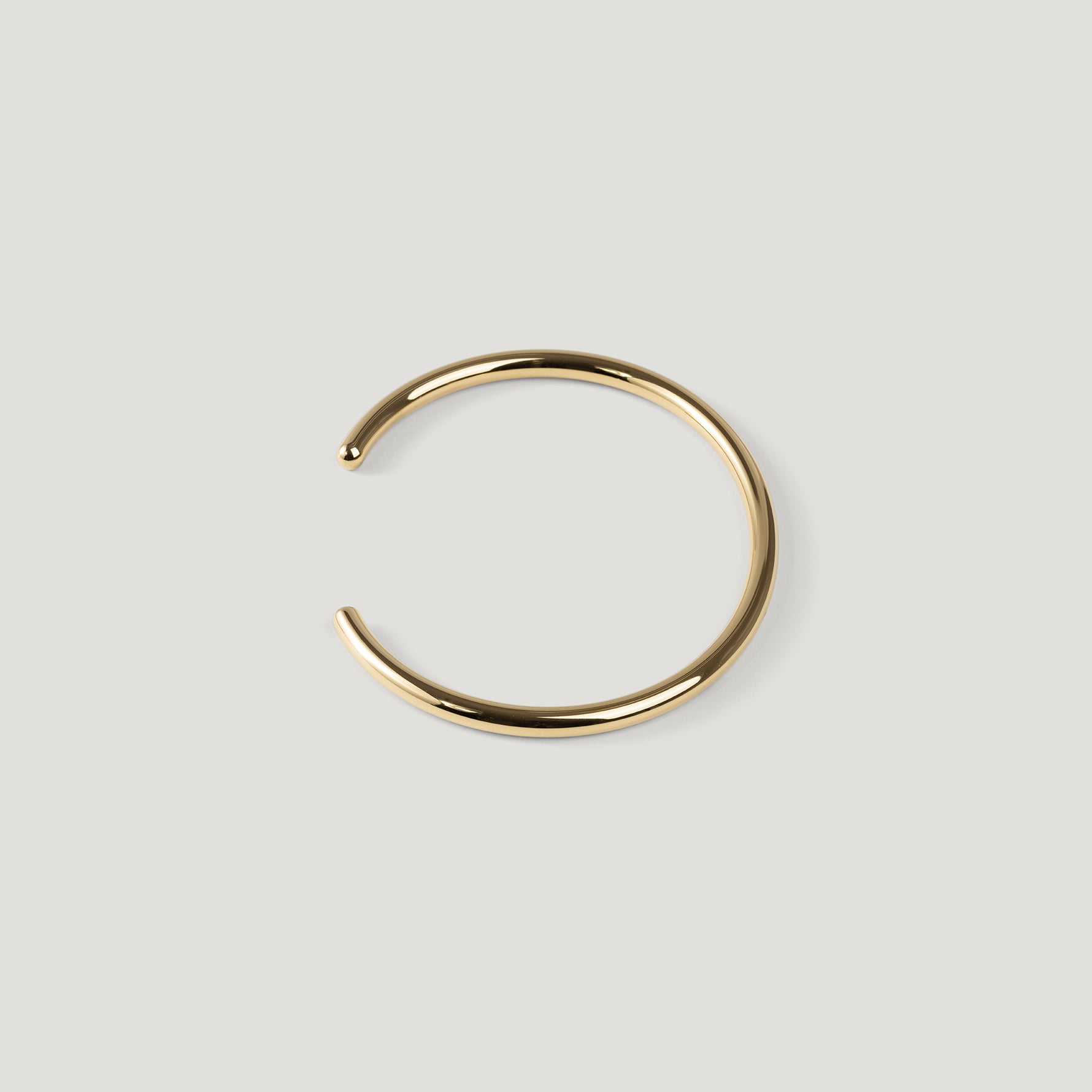 Gold open cuff bangle with rounded wire and ball tip, opening angled to the left.