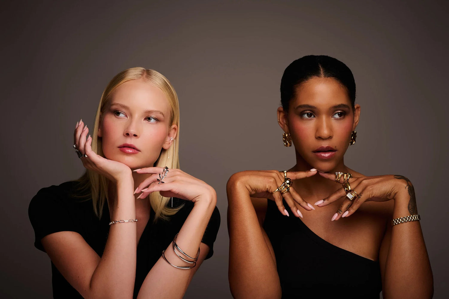 Two women modeling designer rings, bracelets, earrings and contemporary jewelry on neutral background