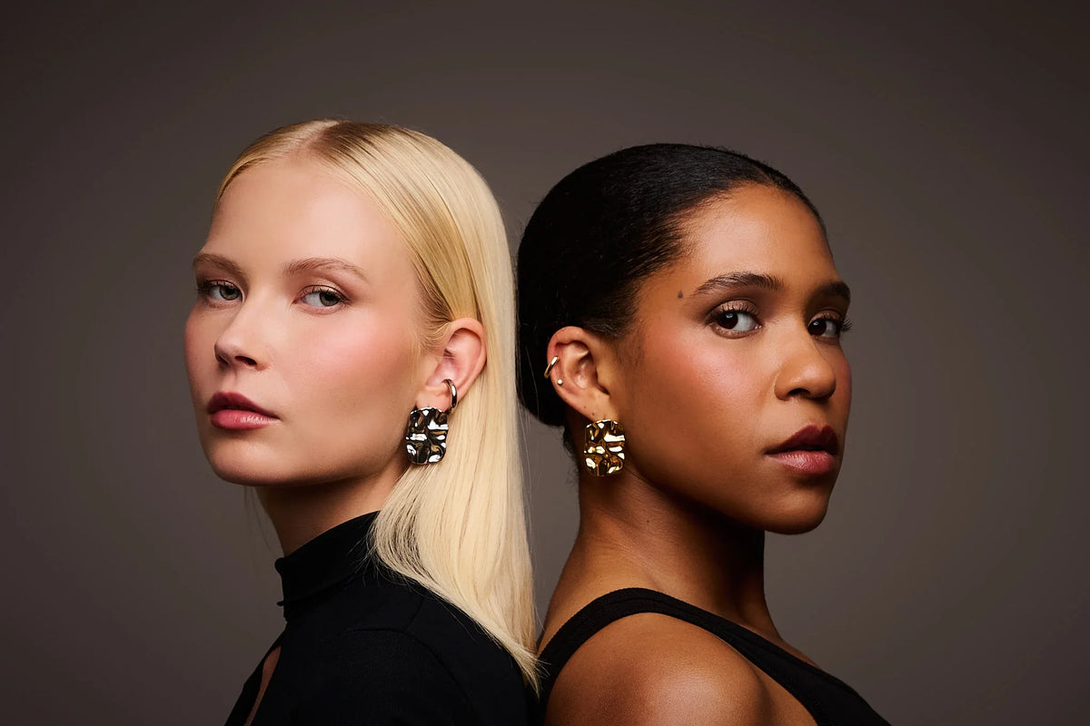 Two women wearing bold, sculptural metal earrings against a neutral background