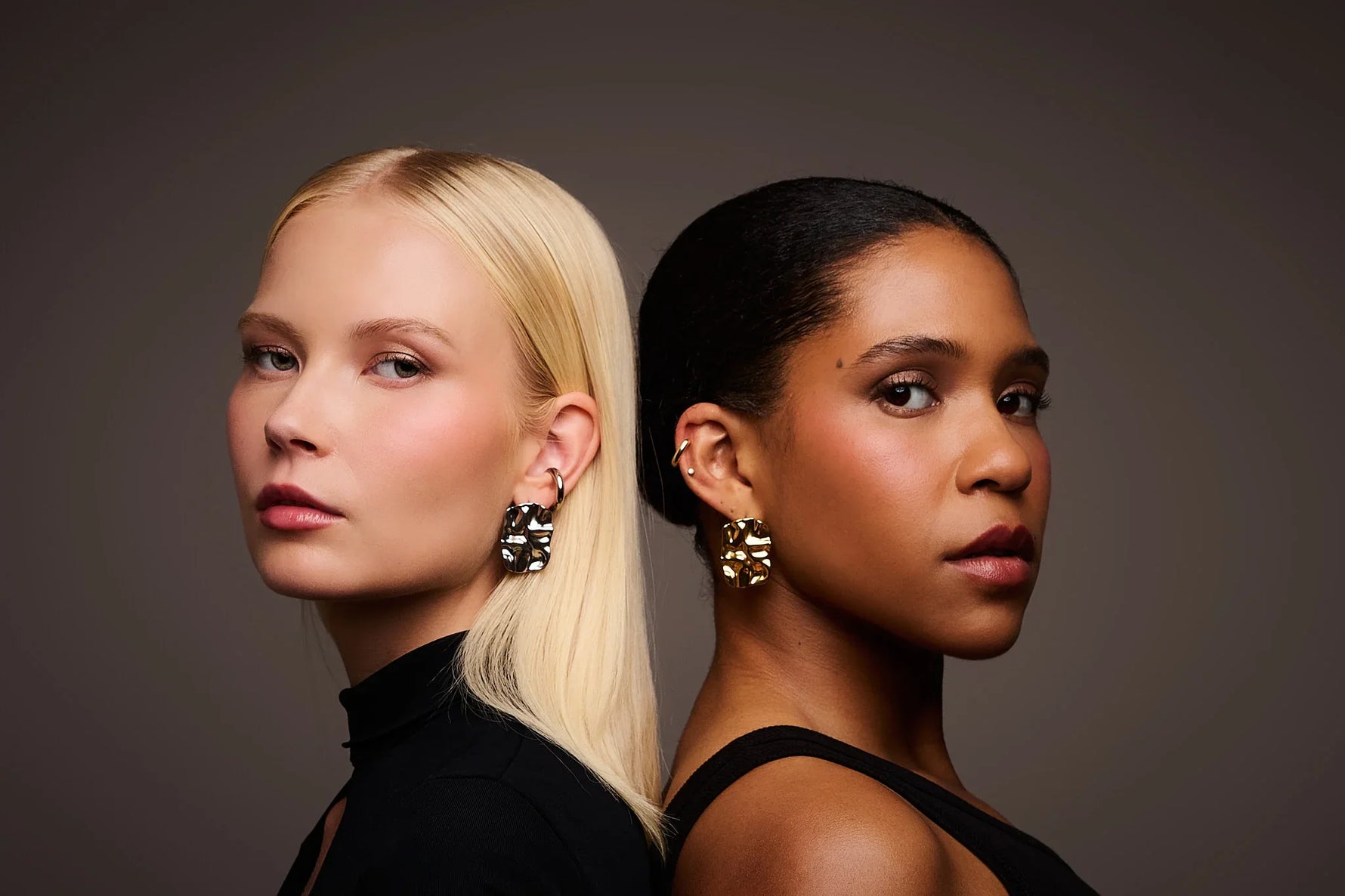 Two women wearing bold, sculptural metal earrings against a neutral background