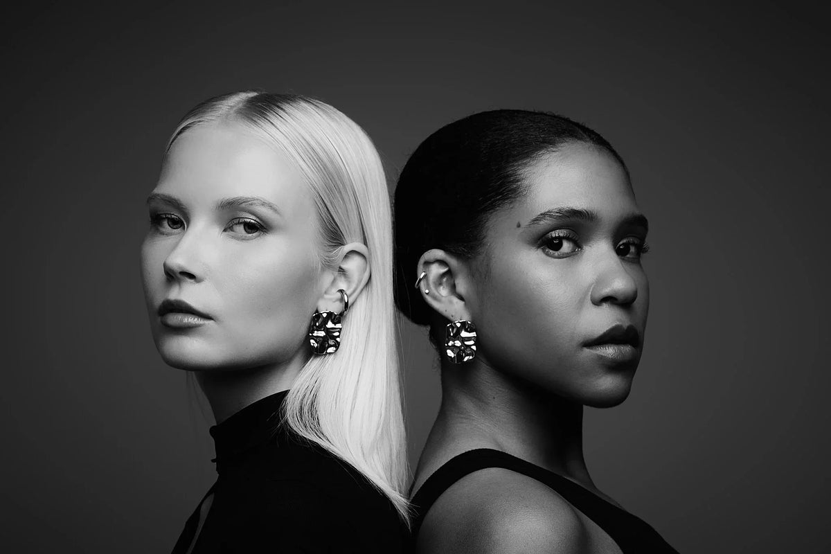 Two women in profile wearing large, modern statement earrings, black and white studio portrait