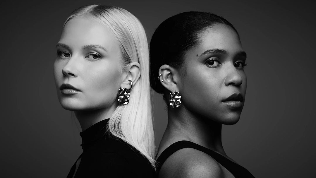 Two women wearing statement sculpted earrings in a black and white studio portrait