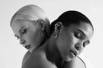 Two women wearing contemporary earrings in a minimalist, black and white studio photo.