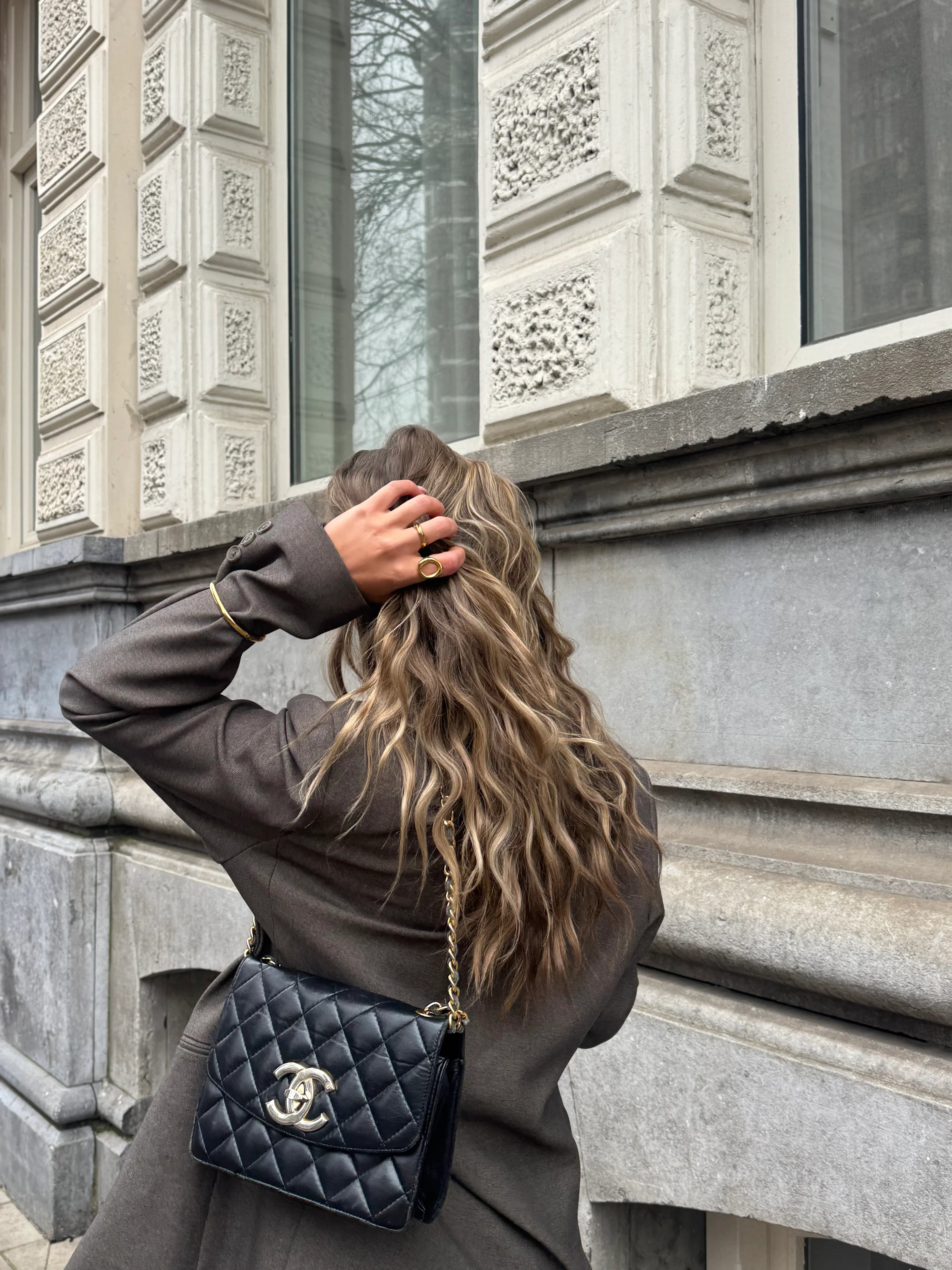 Woman with wavy hair wearing gold rings and a black quilted handbag outdoors