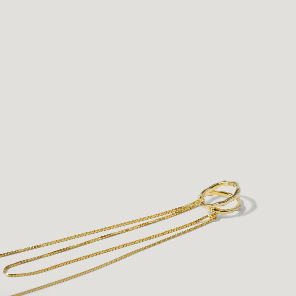 Minimalist gold necklace with two interlocking textured rings on a white background