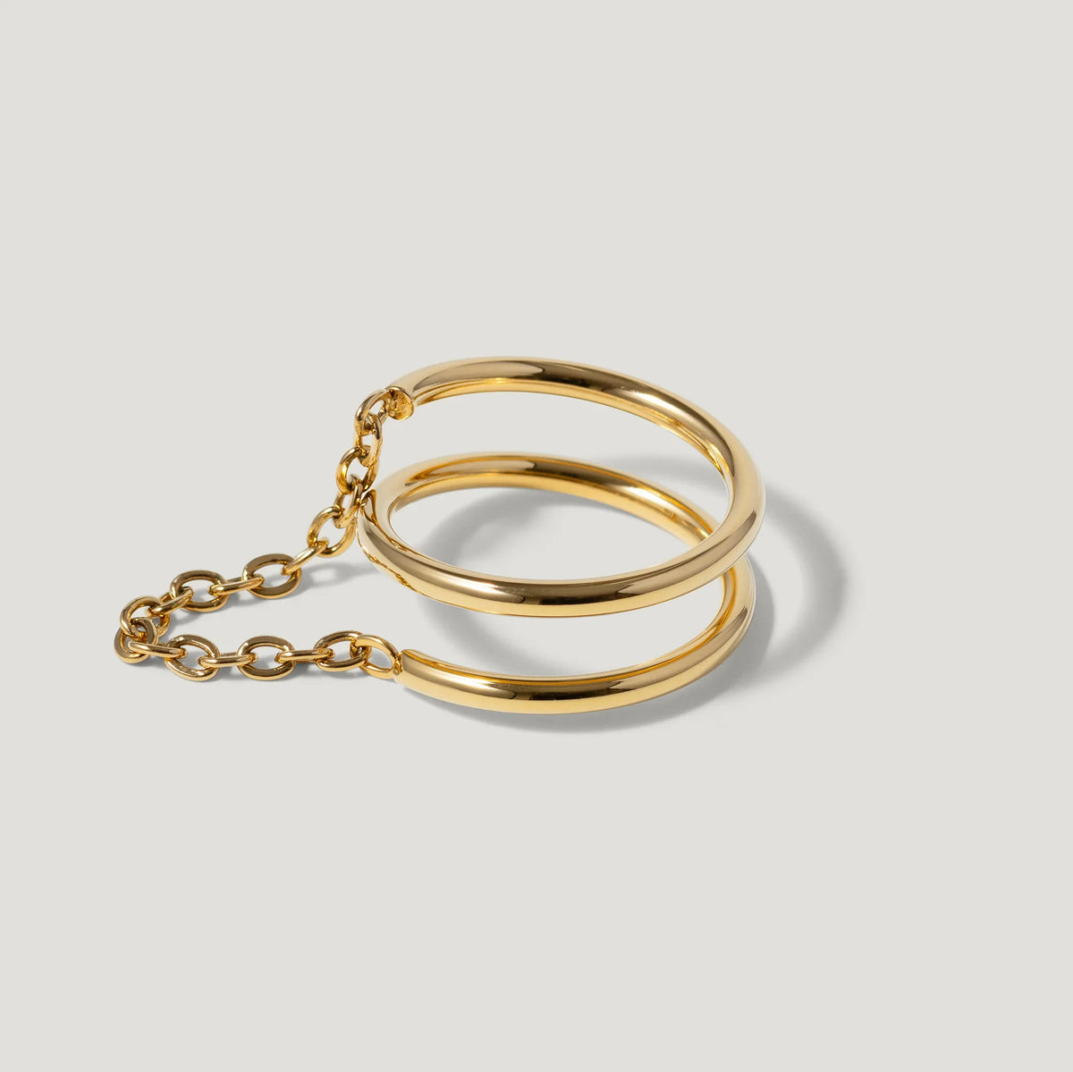 Minimalist gold double band bracelet with chain detail on light background
