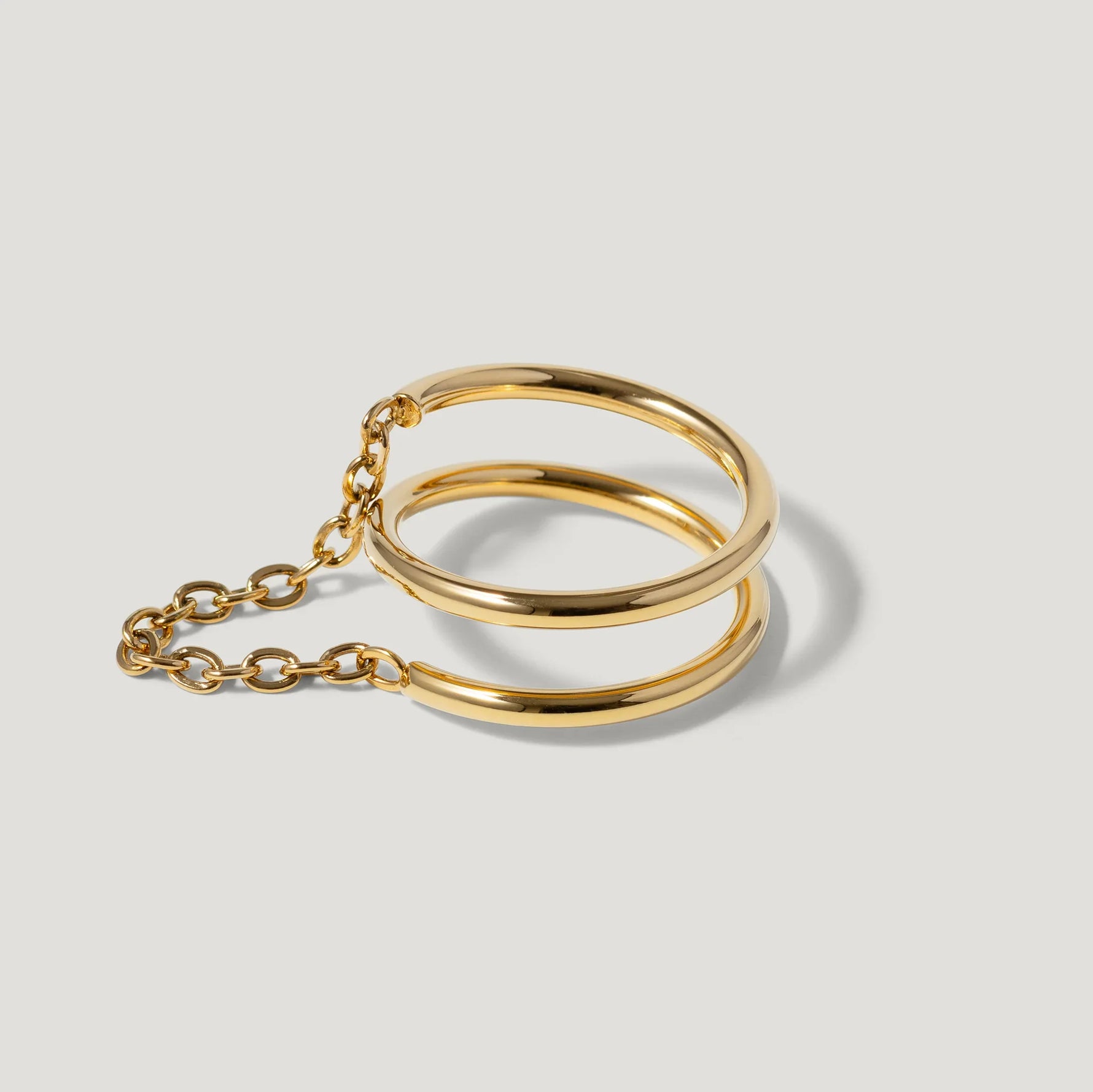 Minimalist gold double band bracelet with chain detail on light background