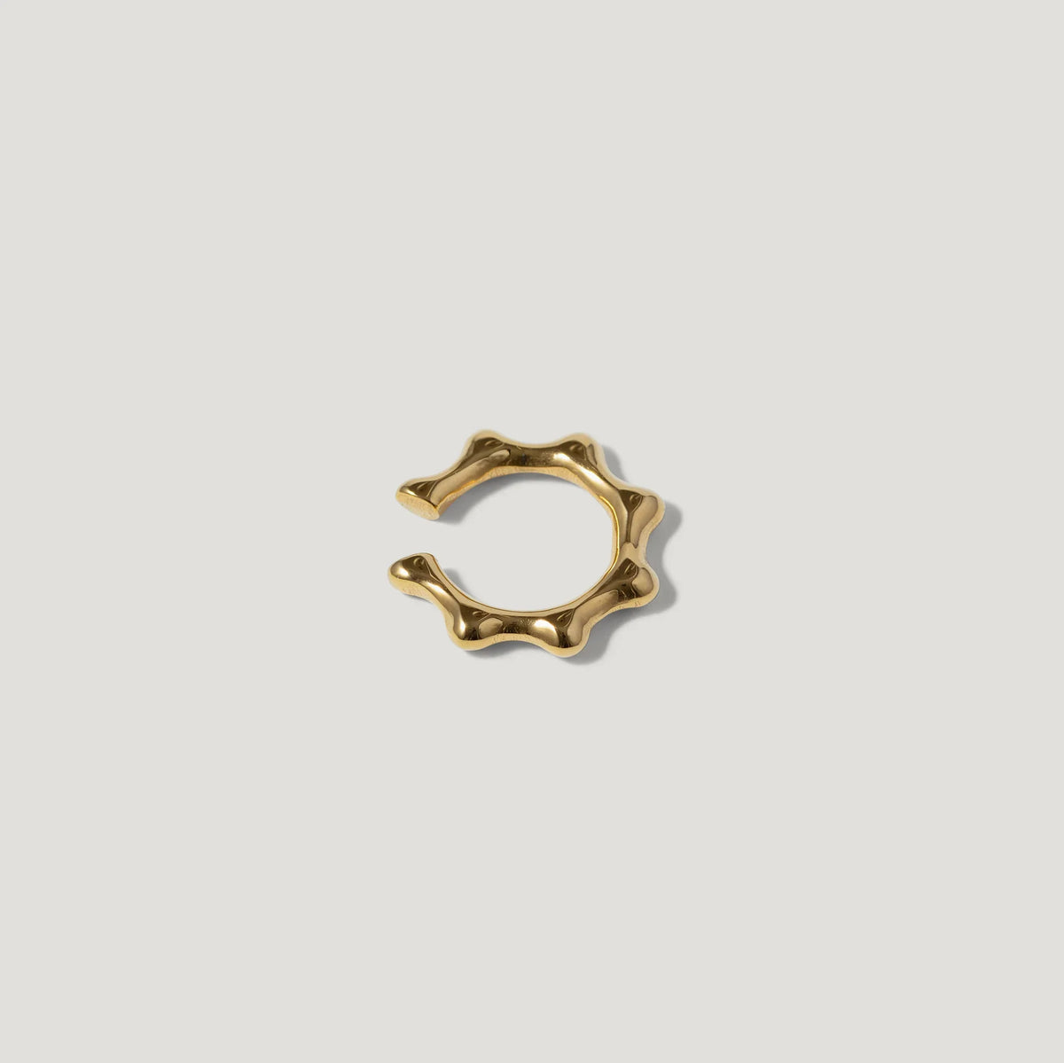 Gold ear cuff with wavy, sculptural design on white background