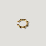 Gold ear cuff with wavy, sculptural design on white background