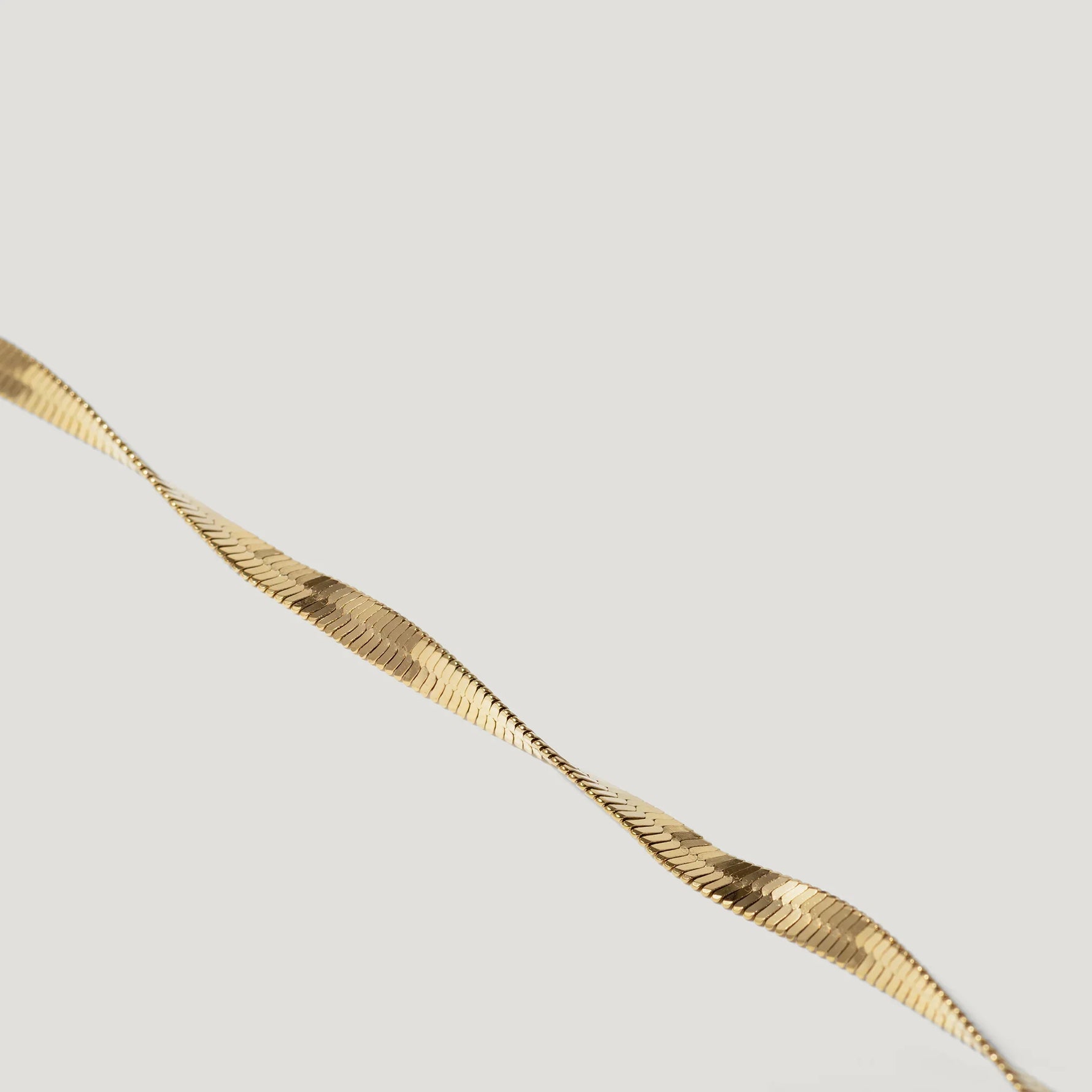 Close-up of a twisted gold herringbone chain necklace on a white background