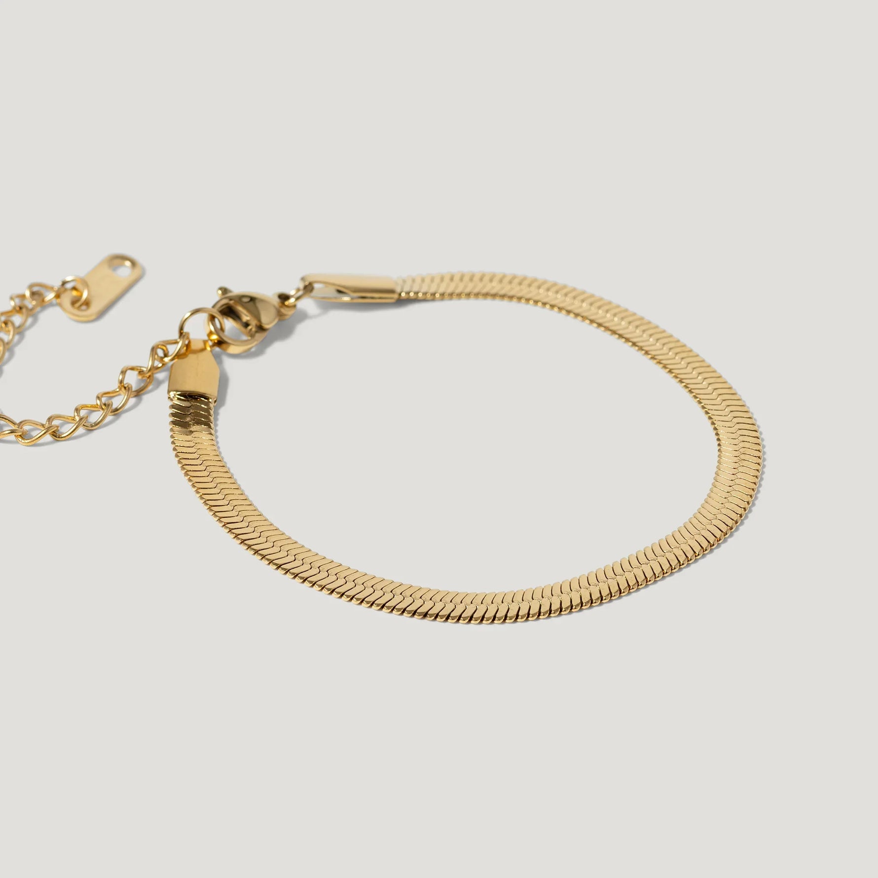 Gold herringbone chain bracelet with adjustable clasp on white background.