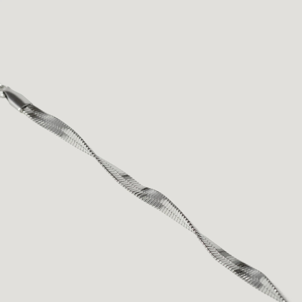 Close-up of a twisted silver herringbone chain necklace on a white background