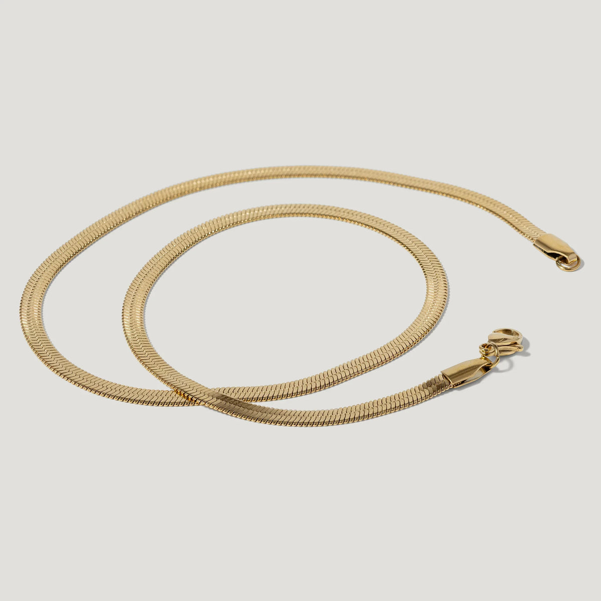 Gold herringbone chain necklace with lobster clasp on white background
