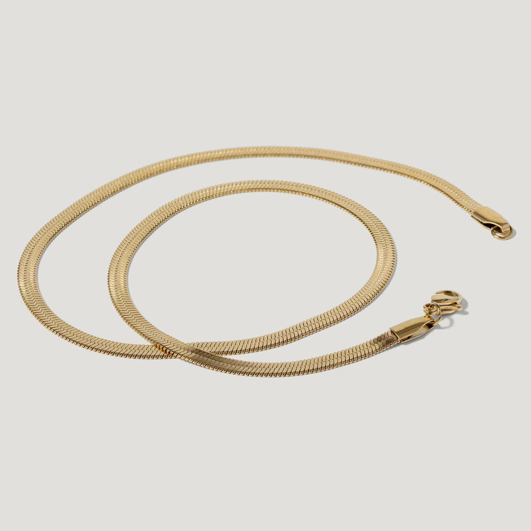 Gold herringbone chain necklace with lobster clasp on white background