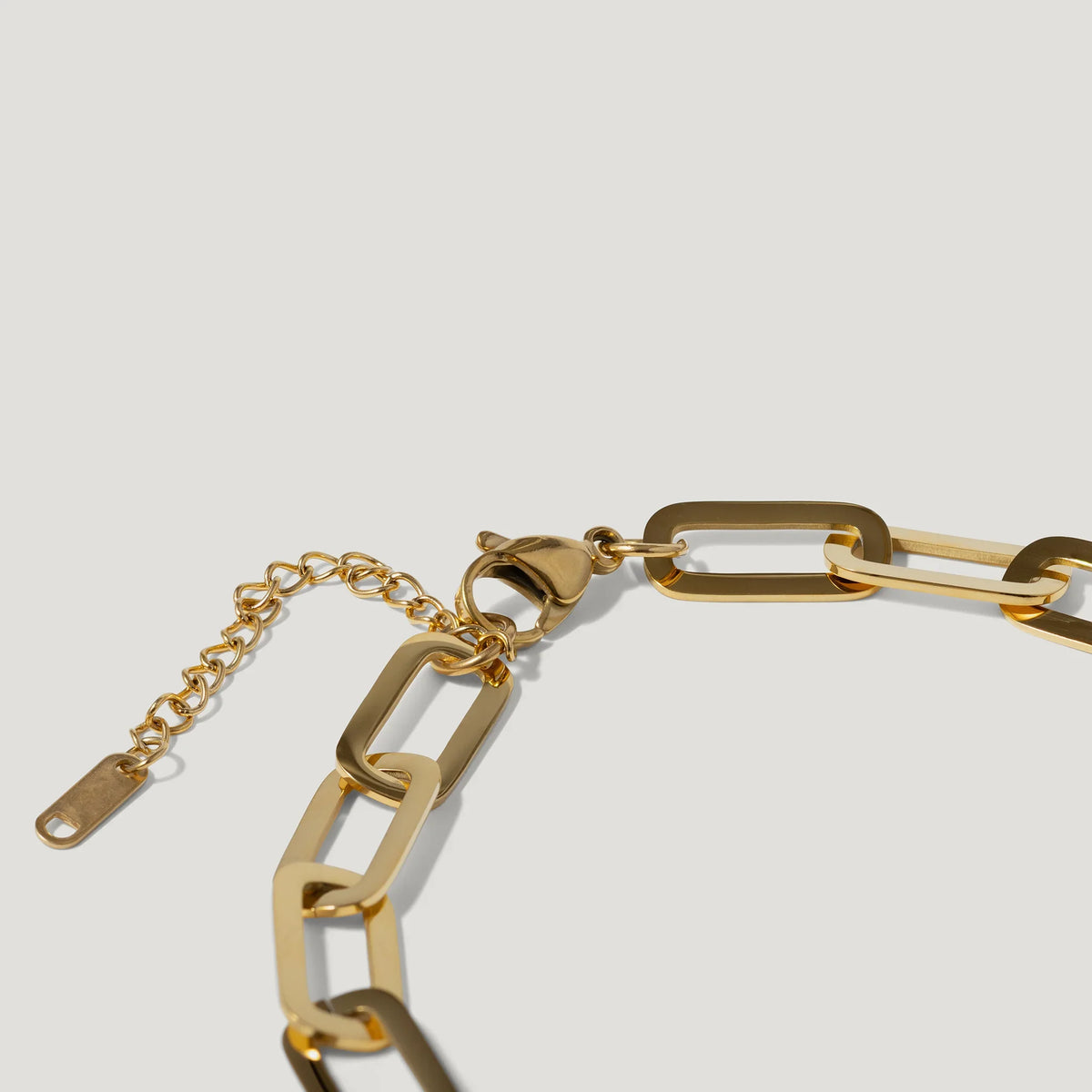 Gold chain link bracelet with rectangular links and lobster clasp on a white background