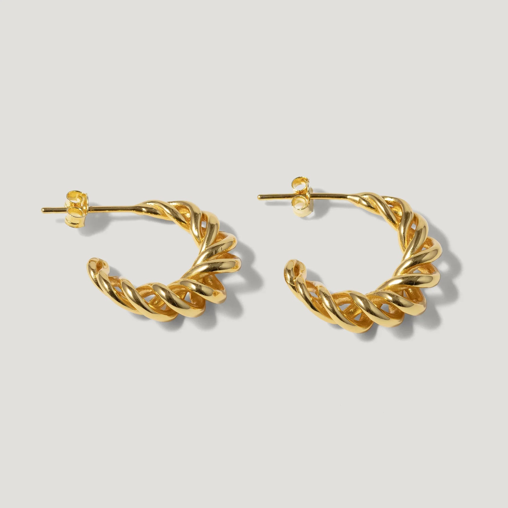 Gold twisted hoop earrings on a light background, elegant jewelry design