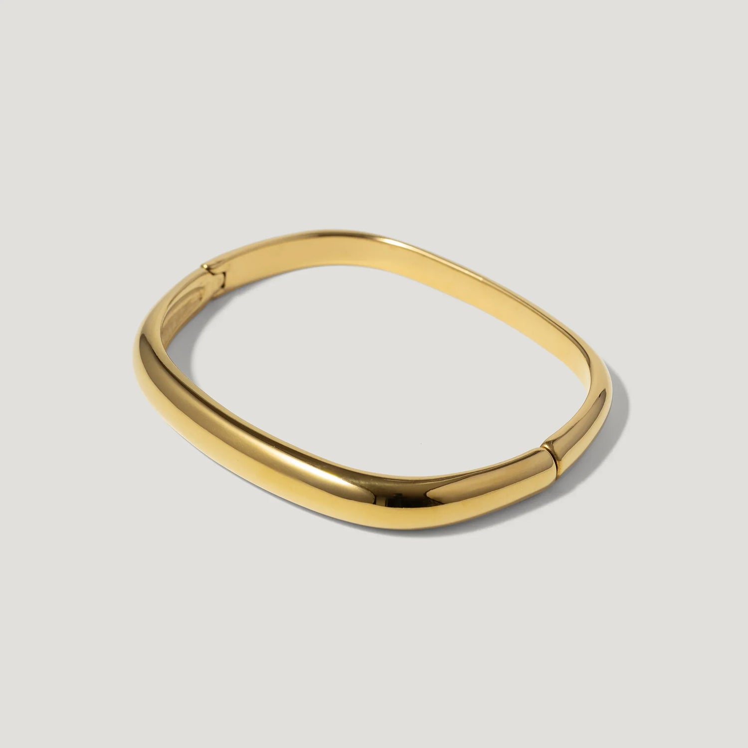 Minimalist gold bangle bracelet with rounded square shape on a light background