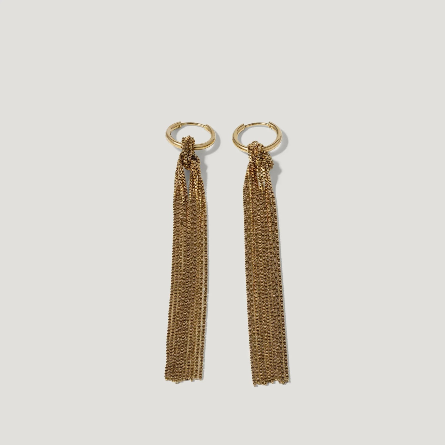 Gold hoop earrings with long chain tassels on white background