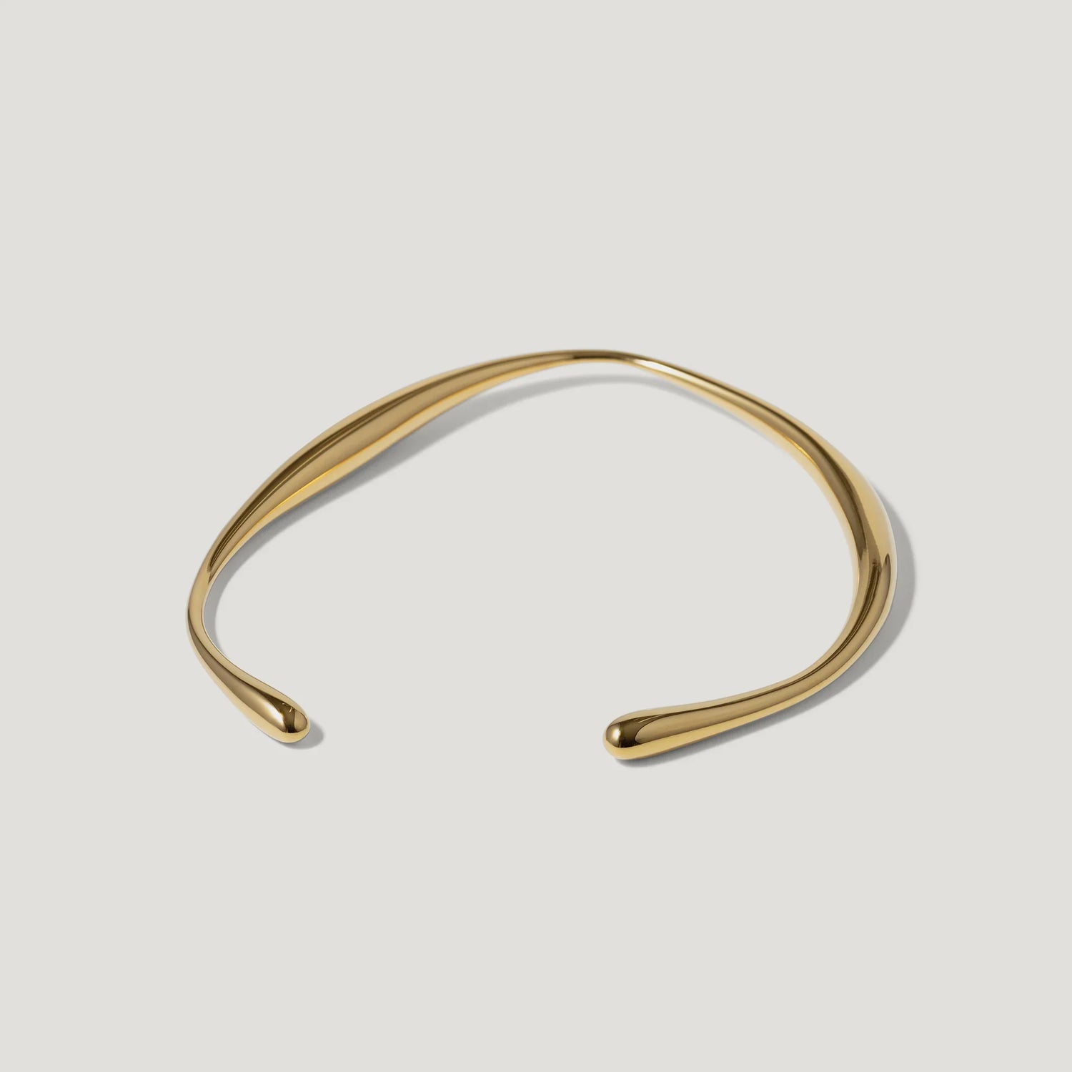 Minimalist gold open cuff bracelet with smooth, curved design on white background