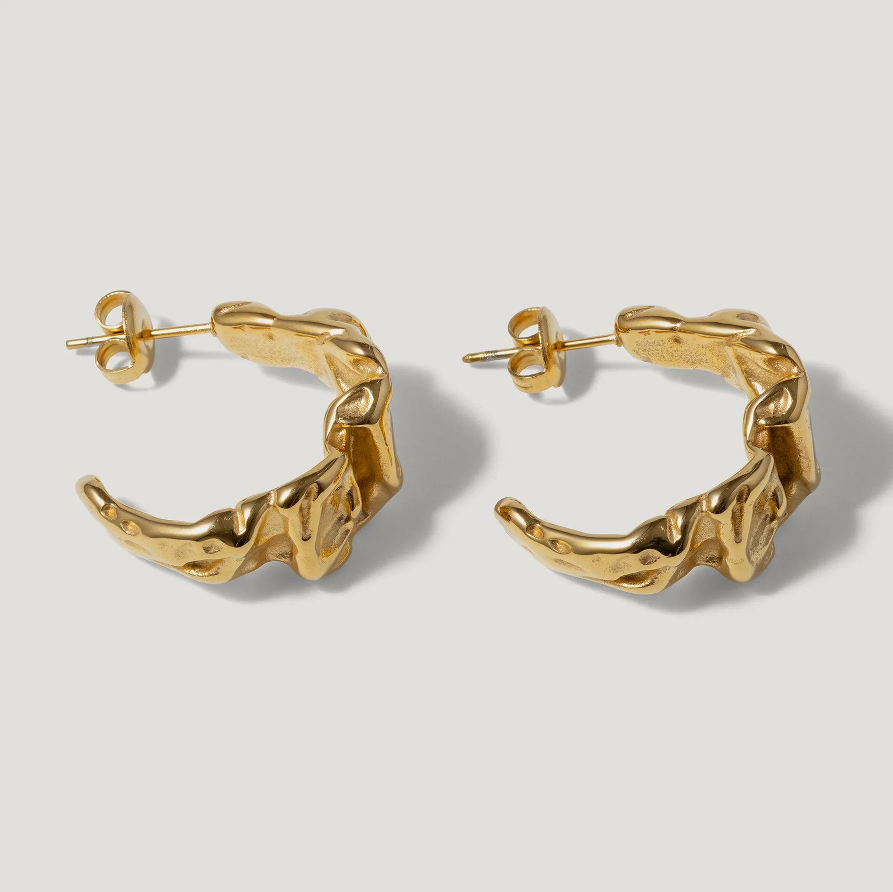 Pair of textured gold hoop earrings with organic, sculptural design on white background