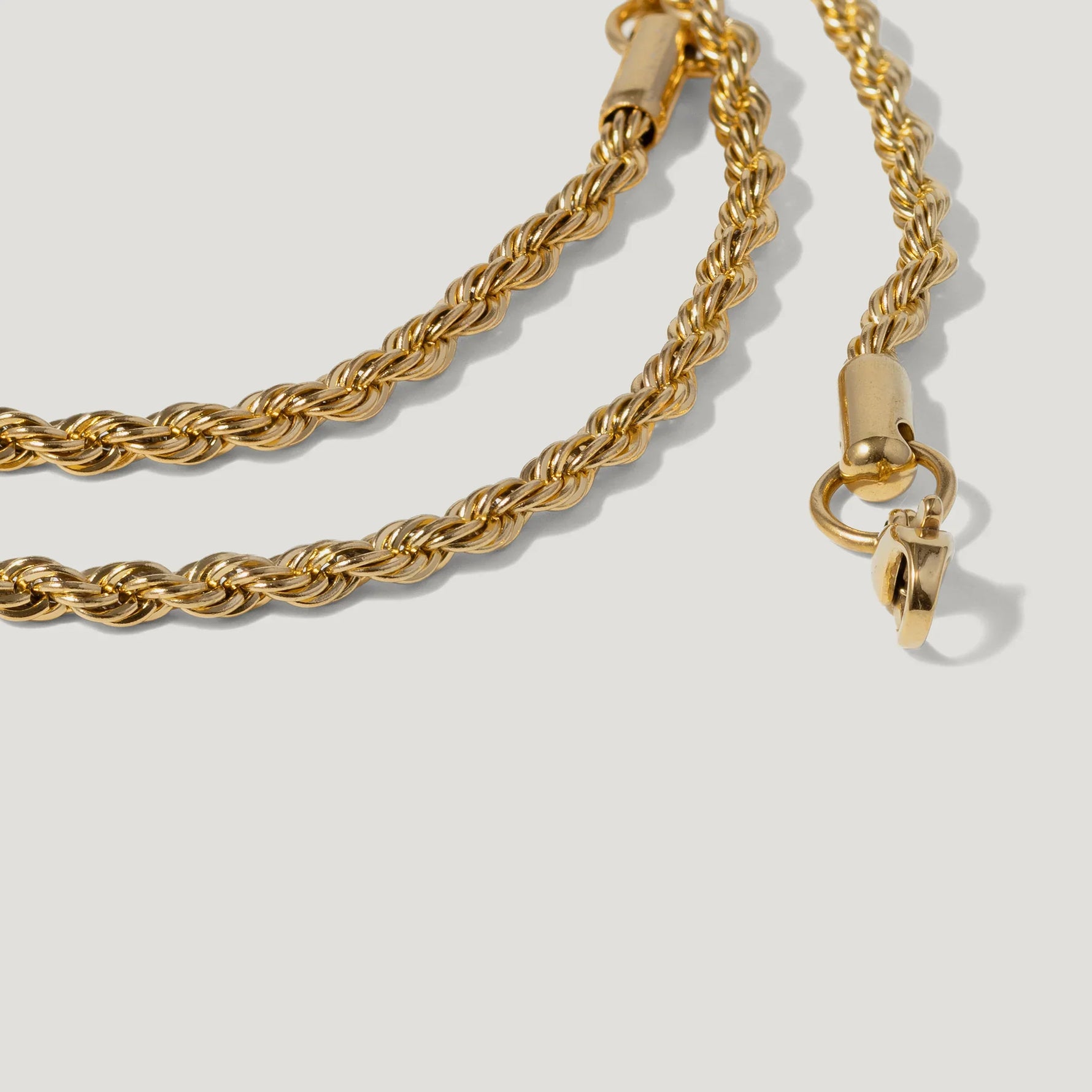 Close-up of a twisted gold rope chain necklace with clasp on a light background